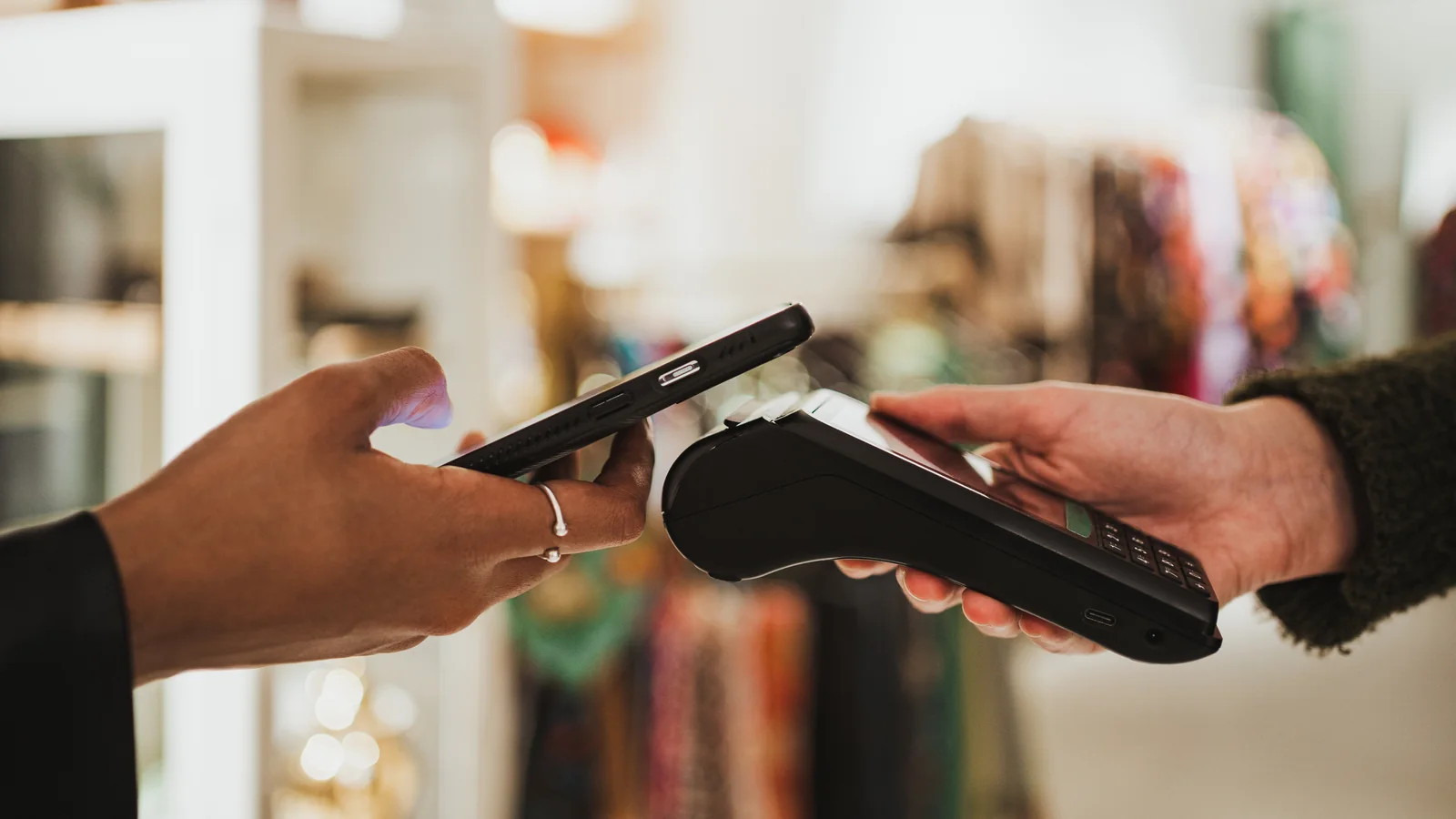 A customer tapping their phone against a handheld card terminal held by a shop assistant